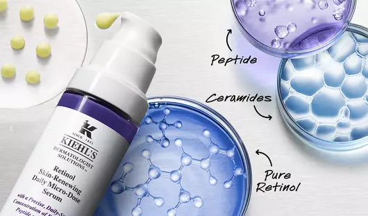 Eine elegante Anordnung von Laborutensilien, darunter Reagenzglaser mit blauen und lila Flussigkeiten sowie eine Flasche mit Hautpflegeprodukten auf einer silbernen Oberflache.