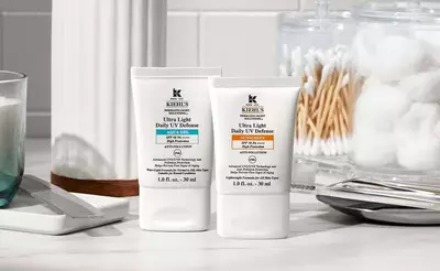 Zwei Kiehl's Sonnencremes auf einem Tisch, umgeben von Kosmetik-Utensilien und Baumwollprodukten.