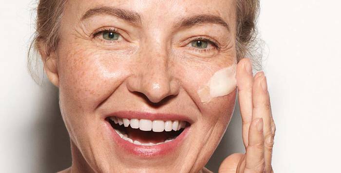 Frau cremt sich lachend die Wange ein