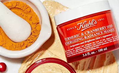 Kiehl's Gesichtmaske mit Kurkuma und Cranberry-Samen fur strahlende Haut, umgeben von Zutaten und einer Morser.