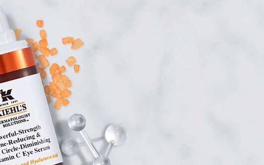 Ein Bild von Kiehl's Hautpflegeprodukten auf marmoriertem Hintergrund, einschließlich einer Serumflasche und einer Tube. Dekorative Elemente wie Lavendel und kleine Sterne sind ebenfalls zu sehen.