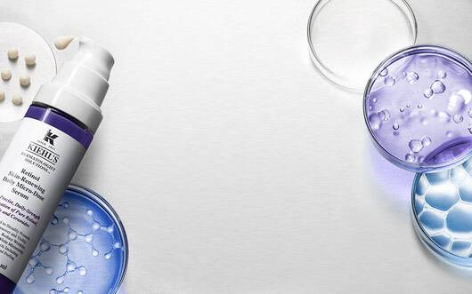Alt-Text: Eine kosmetische Flasche befindet sich im Mittelpunkt, umgeben von Reagenzglasern und transparenten Gelen in verschiedenen Farben, die die wissenschaftliche Grundlage fur Hautpflegeprodukte darstellen.