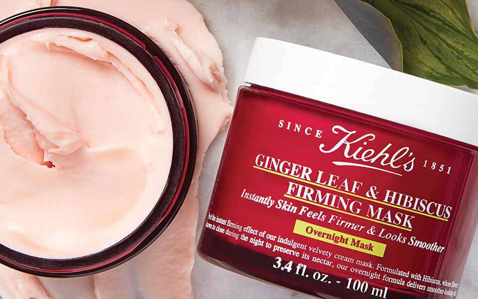 Eine marmorierte Oberflache mit Kiehl's Hautpflegeprodukten, darunter eine feuchtigkeitsspendende Creme und ein Gesichtsol, sowie einige gelbe Blutenblatter.