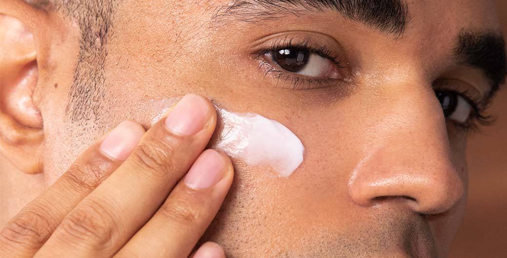 Mann tragt Creme auf das Gesicht auf