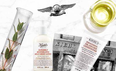 Ein Kiehl's Produktfoto mit Argan-Bodylotion, Ol und einer Apotheke im Hintergrund. Botanische Elemente sind sichtbar.