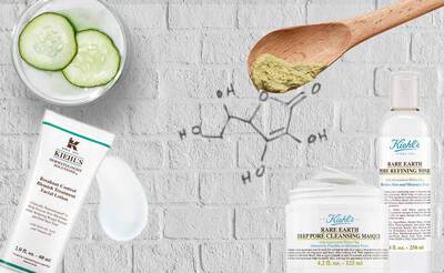 Gesichtspflegeprodukte von Kiehl's mit Gurkenstucken und einer Holzschaufel auf einem Backstein-Hintergrund.