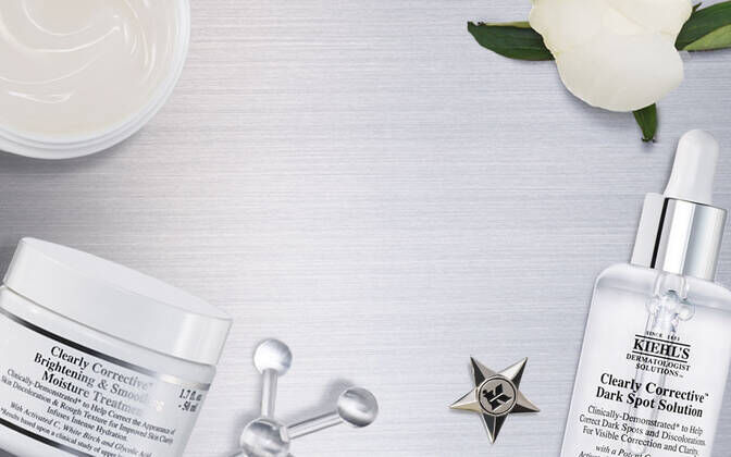 Produktarrangement mit Kiehl's Hautpflegeartikeln auf einer metallischen Oberflache, umgeben von Blumen- und Pflegeutensilien.