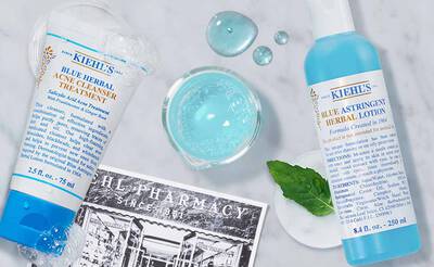 Produkte von Kiehl's: Blauer Krauter-Akne-Reiniger und astringierende Lotion auf einem hellen Hintergrund mit Wasserblasen.