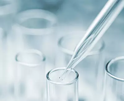 Eine Pipette, die uber einem Reagenzglas schwebt, vor unscharfem Hintergrund.