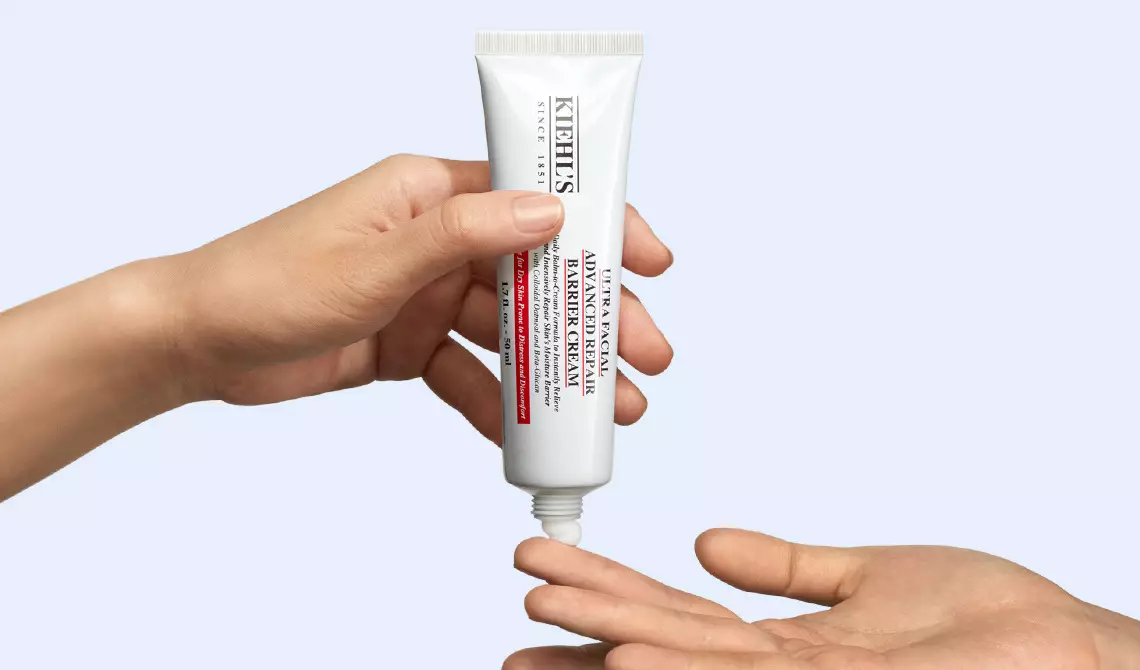 Eine Hand halt die Tube der Ultra Facial Advanced Repair Barrier Cream mit kolloidalem Hafer und appliziert etwas Creme auf eine andere Hand.