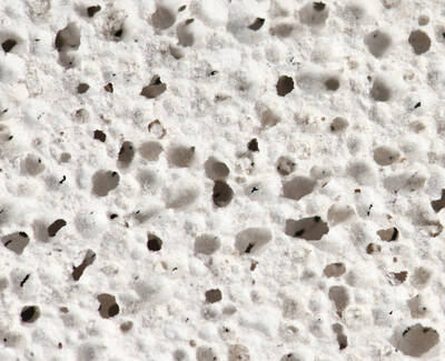 Close-up of a porous, white surface with numerous small holes and an uneven texture.