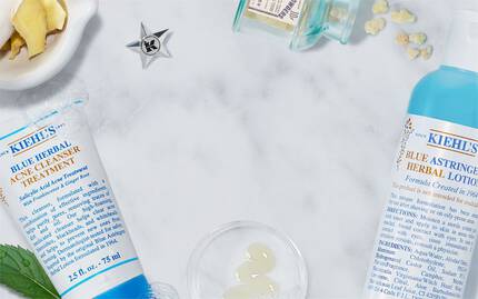 Alt-Text: Eine Anordnung von Kiehl's Hautpflegeprodukten auf einer marmorierten Flache, umgeben von frischen Zutaten wie Minze und Ingwer.