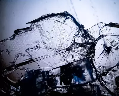 Close-up view of translucent, intricately structured crystals with sharp edges and faint blue highlights, set against a light background.