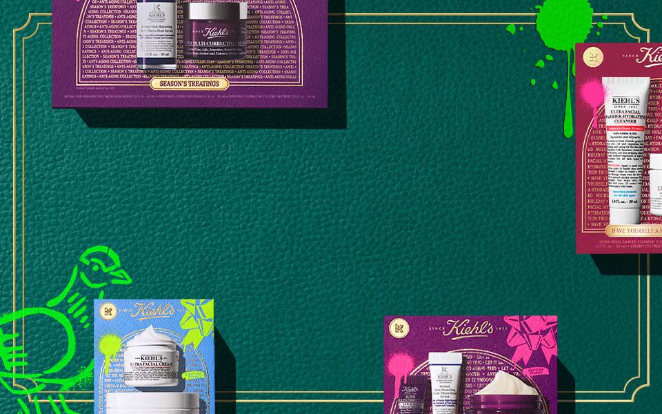 Horizontaler Banner mit dunkelgrunem, strukturiertem Hintergrund und goldenen Rahmenlinien, auf dem bunte Kiehl’s-Geschenkboxen in Pink, Blau und Lila mit Hautpflegeprodukten zu sehen sind. Auf beiden Seiten erscheinen grune, kunstlerische Akzente.